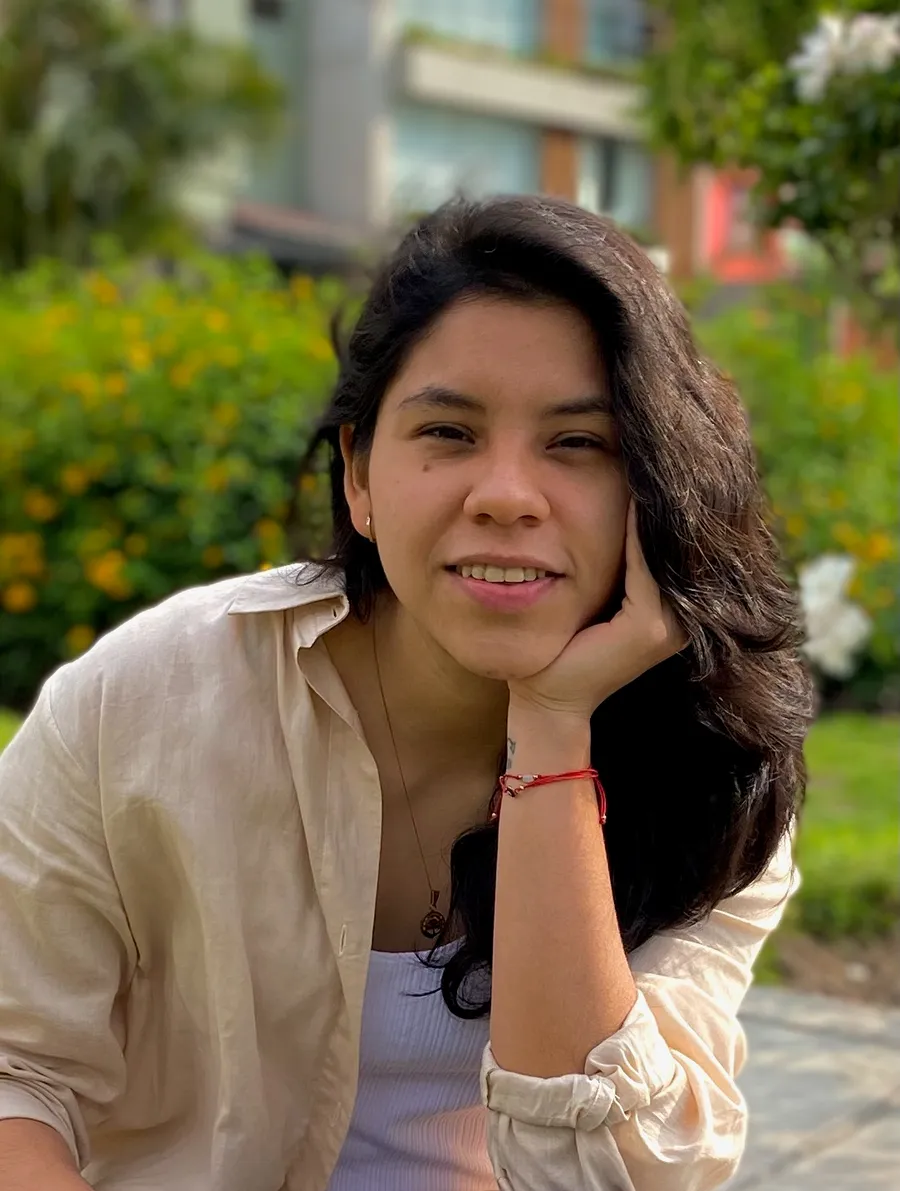 Retrato de Zabrinna Vargas Antinori, sonriente, con camisa clara y la mano apoyada en la mejilla, al aire libre.